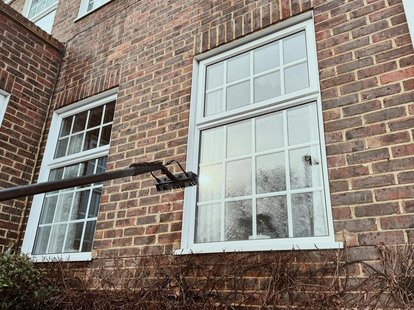 A close-up photograph of a window with pale hard water spots visible in low sunlight, set within a clean white frame on a refined London townhouse exterior
