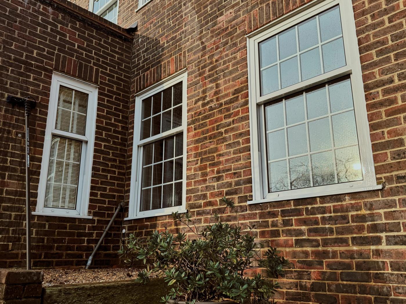 A refined home frontage with clean sash windows, bright white frames, clear paving, clipped planting and a polished front door in soft afternoon light