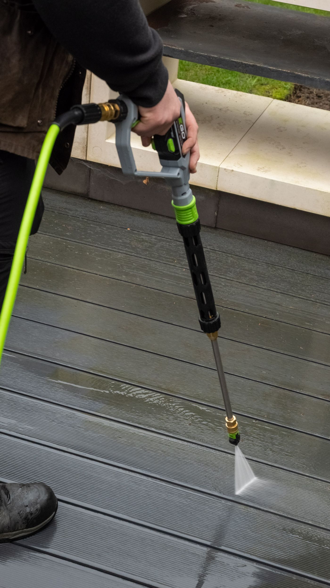 A professional cleaning a block paved driveway with controlled jet washing, the cleaned section visibly brighter and the uncleaned section still dark with grime