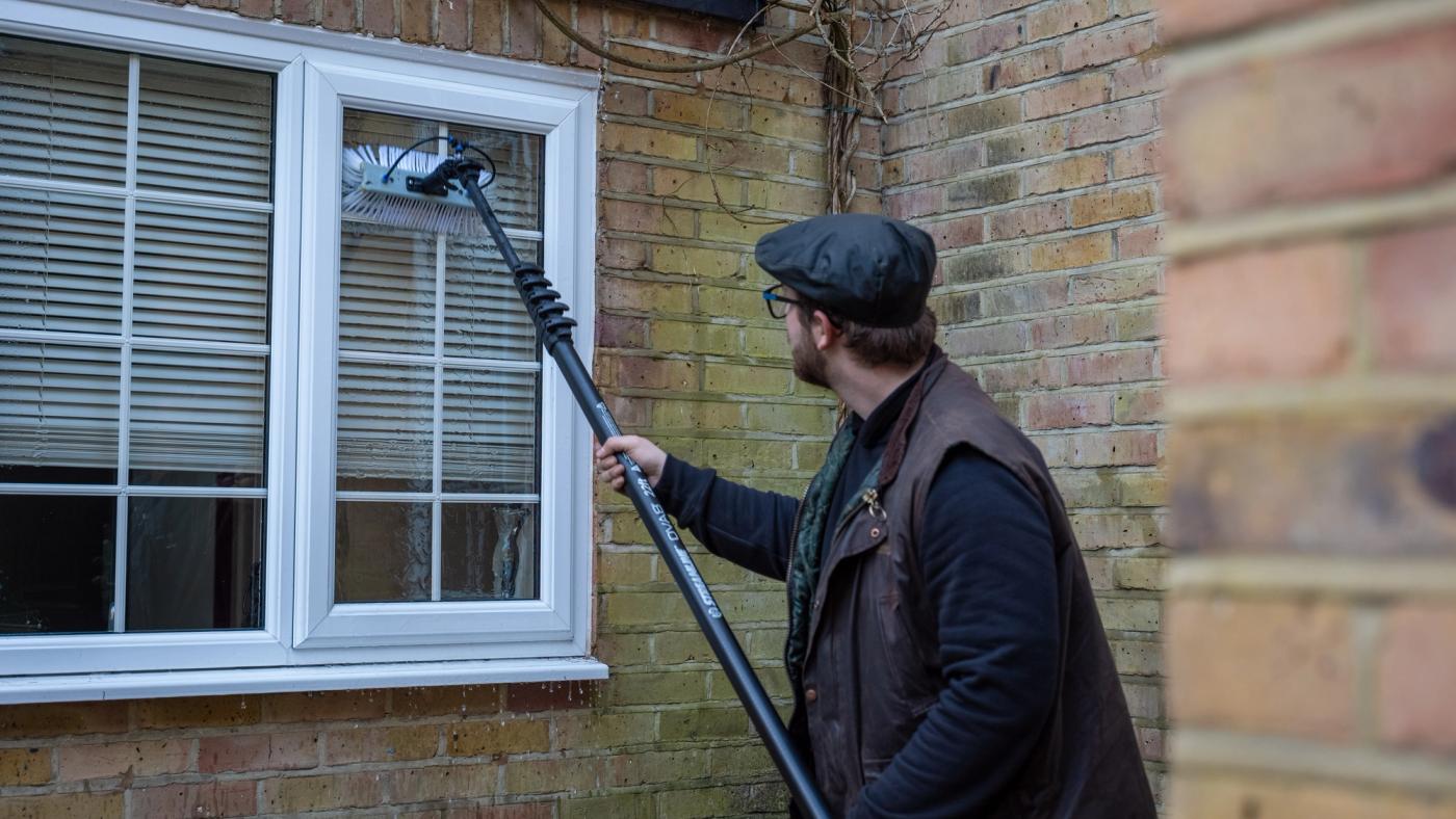A professional pure water pole system cleaning tall sash windows on a Chelsea townhouse, with clear water rinsing the glass and painted frames from the ground