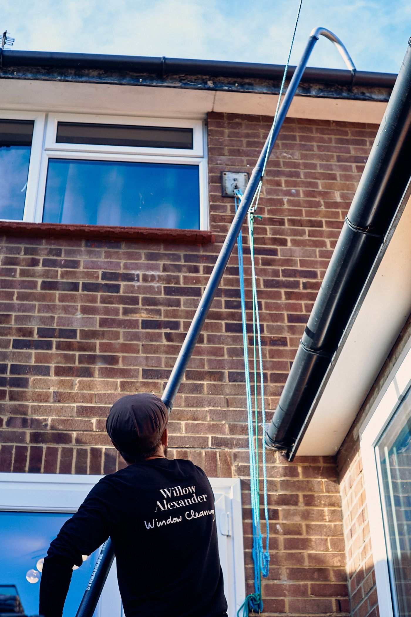 A roofline after gutter clearing, with clean white fascias, clear gutter channels and rainwater flowing properly towards the downpipe