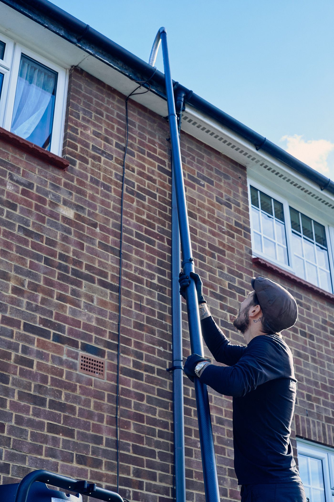 A high-suction SkyVac pole being used from the ground to clear a roofline gutter on a well-kept Kent home, with no ladder resting against the facade