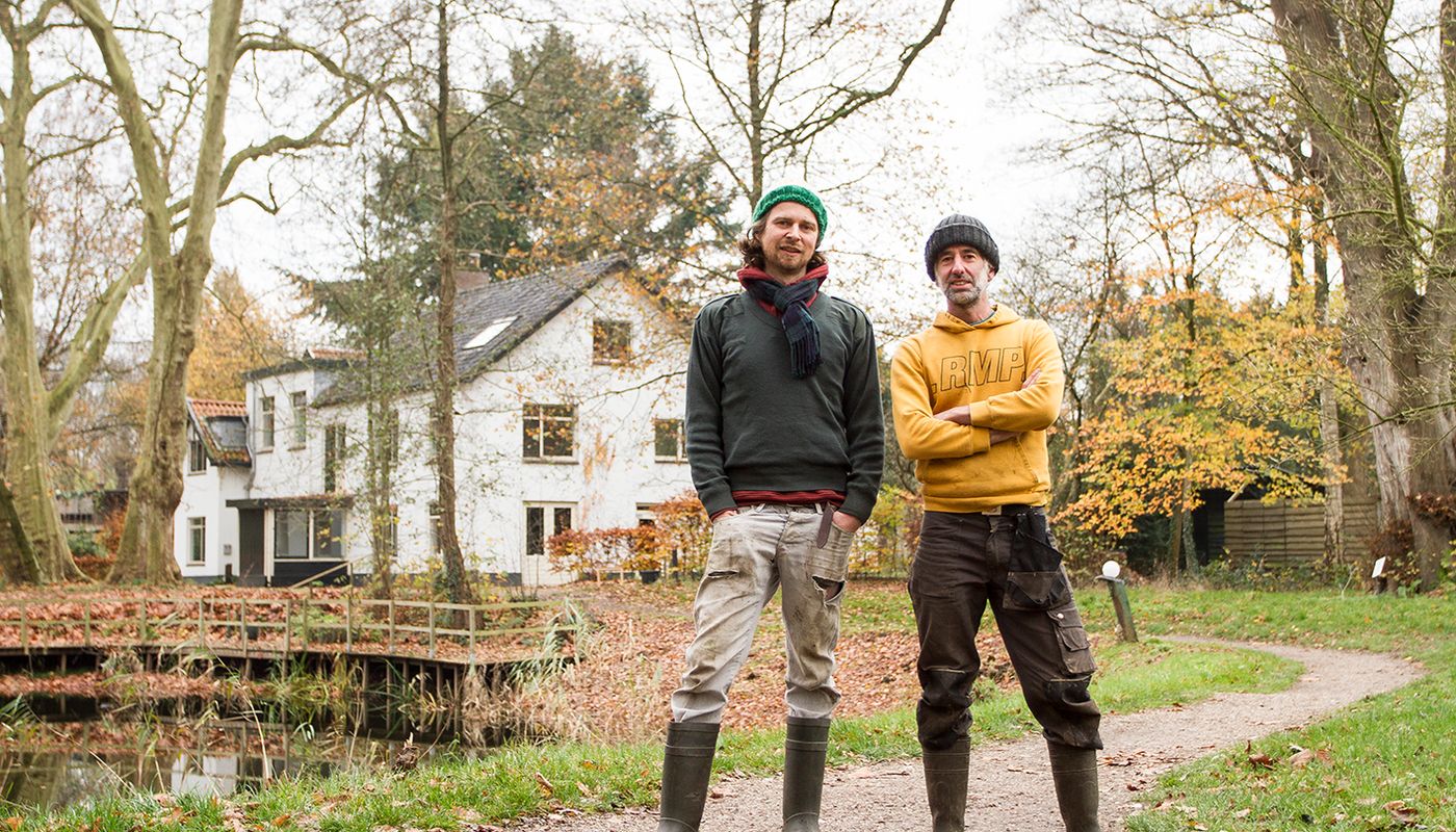 Tuinders Jasper en Dave staan op het pad voor de vijver en het witte koetshuis op Landgoed Kraaybeekerhof.
