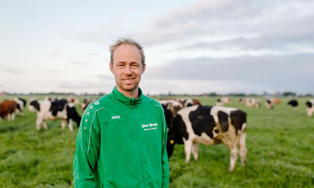 Jaring Brunia staat lachend in het veld met koeien op de achtergrond