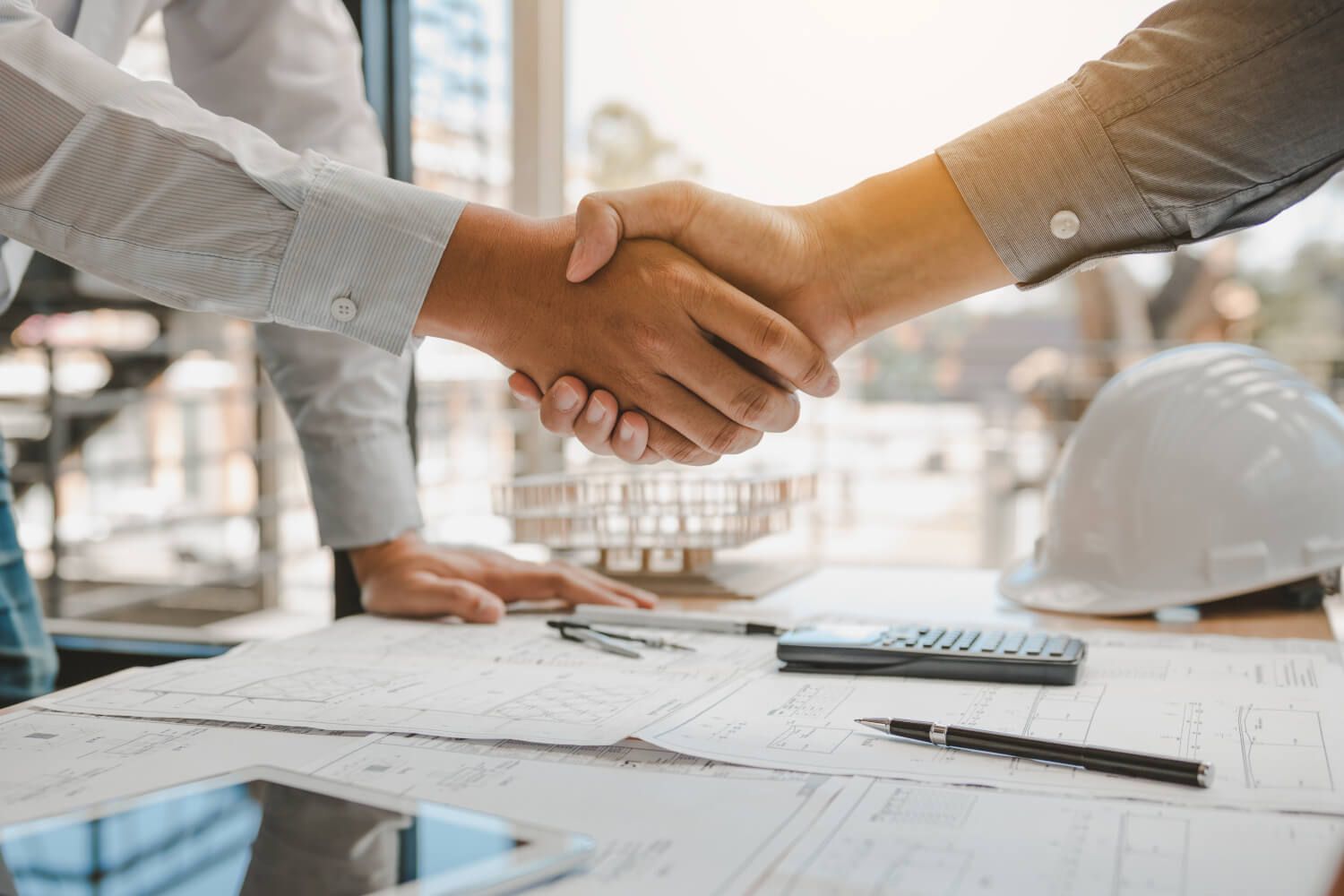 Two construction workers shaking hands over paperwork