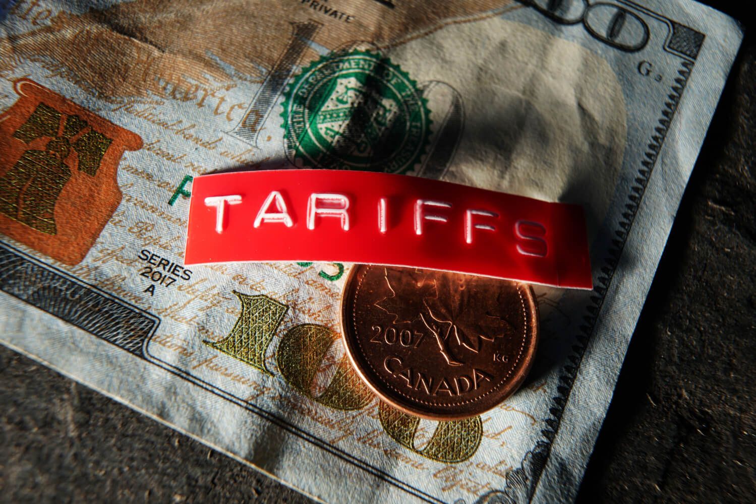 Canada coin and tariff label on a US hundred dollar bill