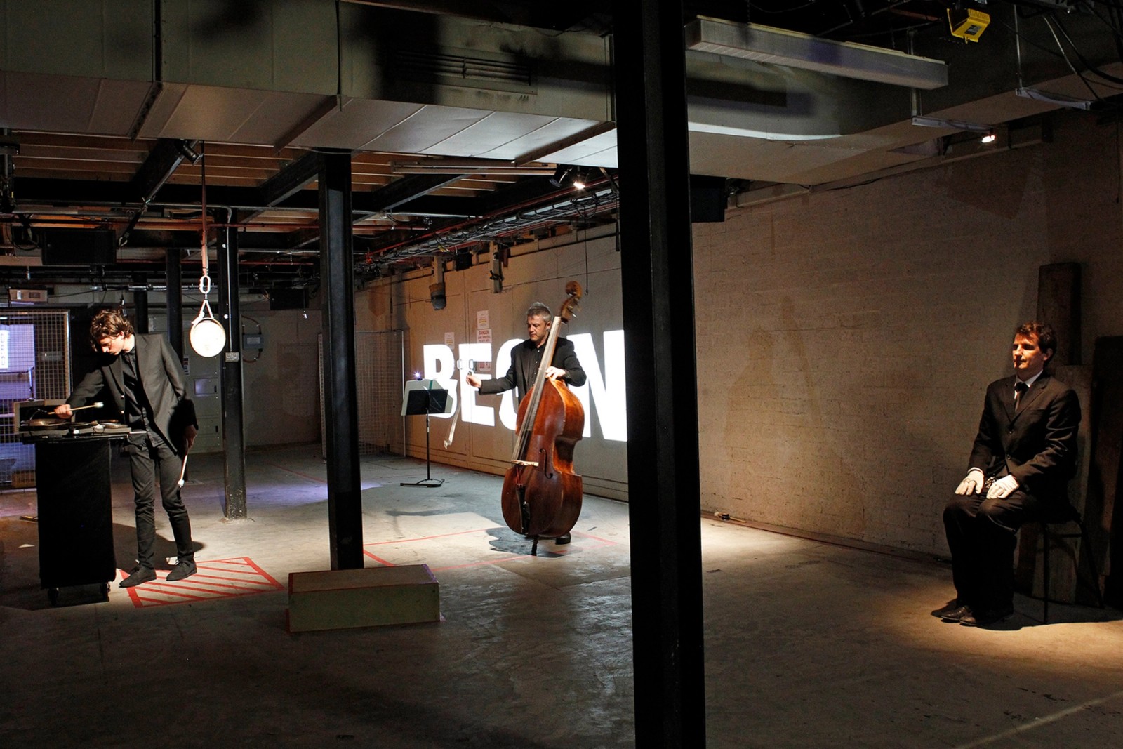 Three performers in an underground space with the word BEGIN projected as part of Captives of the City by Chamber Made