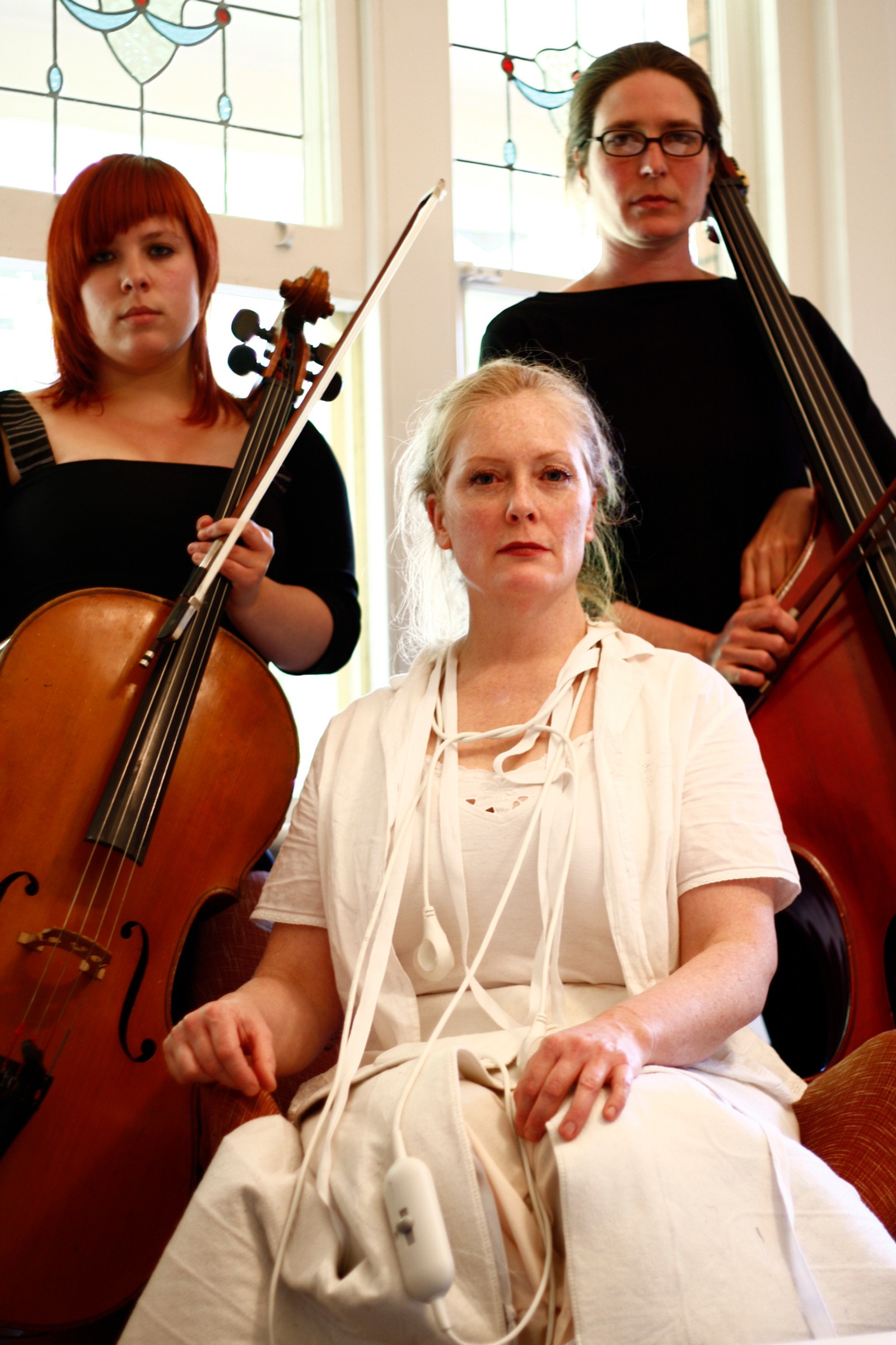Two women with a cello and double bass stand behind a seated woman in white as part of The Itch by Chamber Made