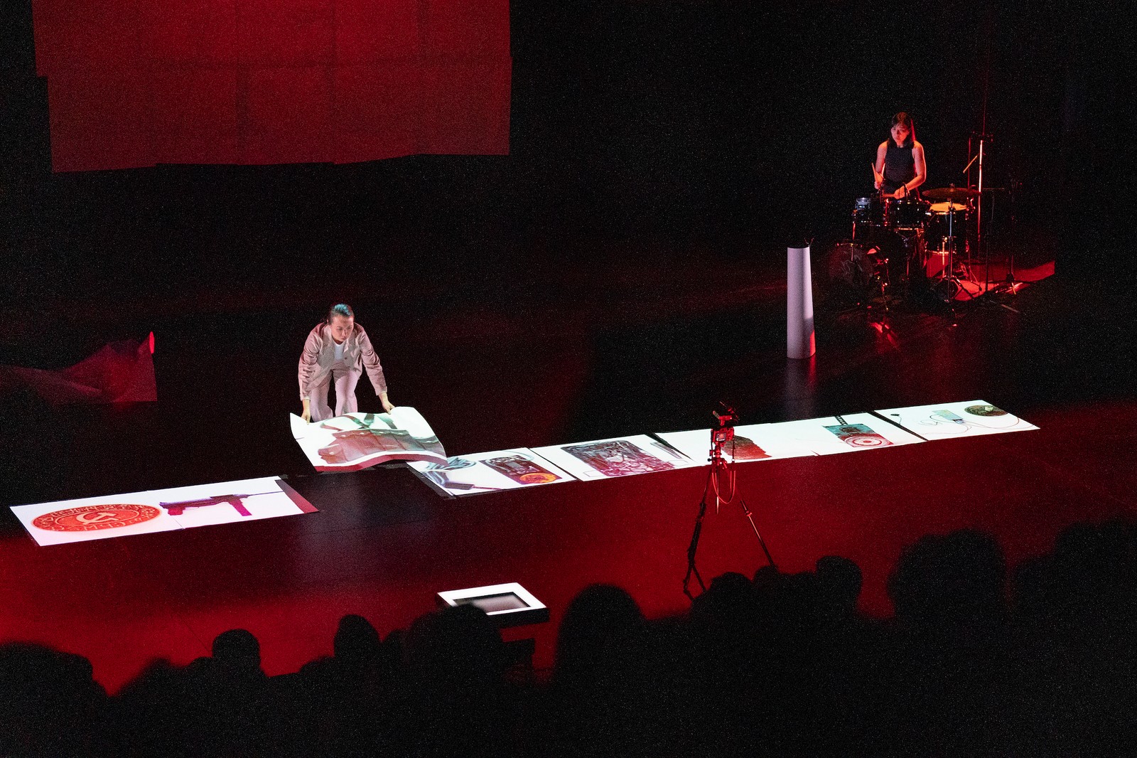 Woman on stage standing above a series of objects projected on the floor as part of One Day We'll Understand.