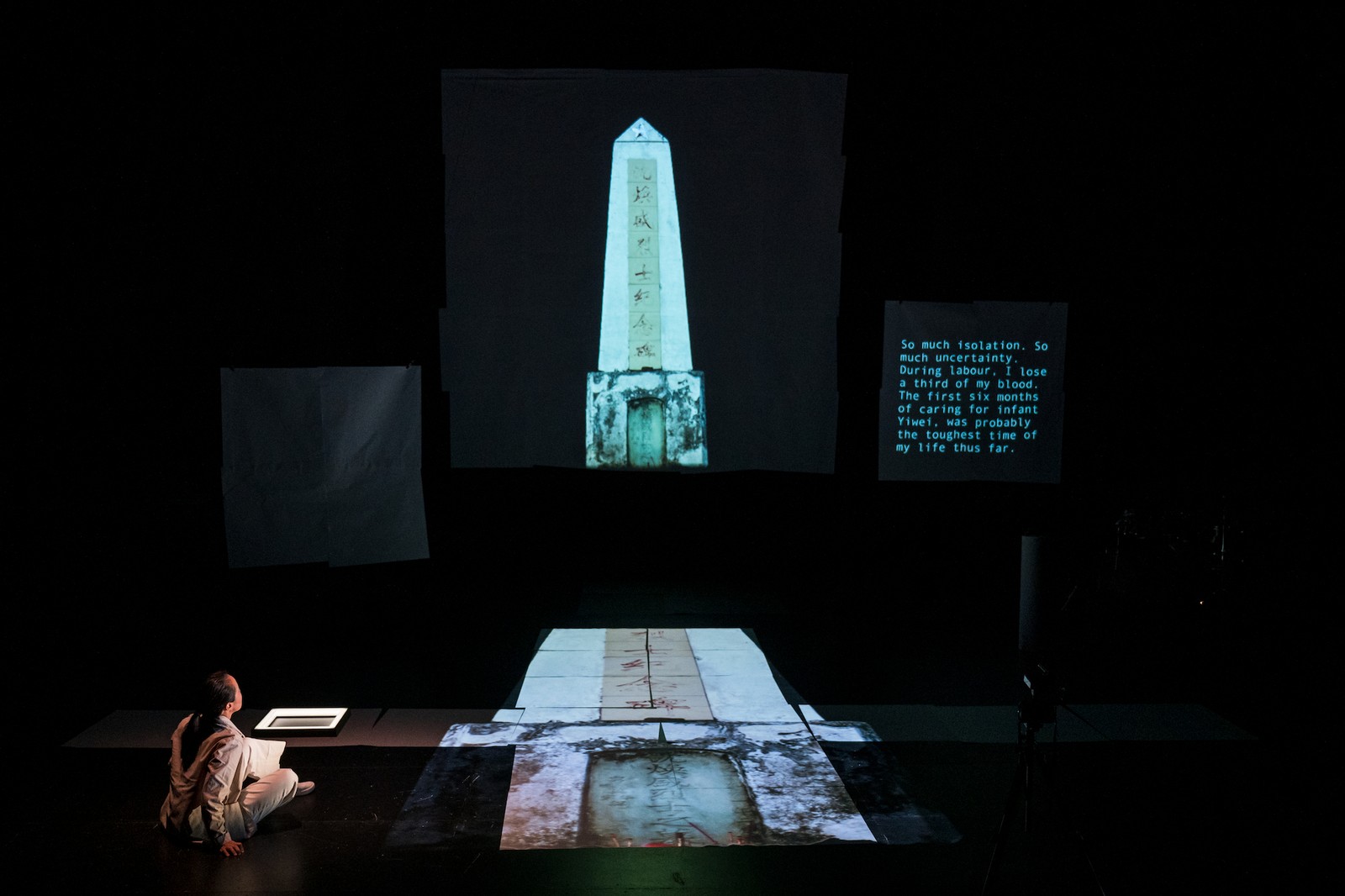 Woman sitting on a dark stage with the projection of a Chinese tomb as part of One Day We'll Understand.