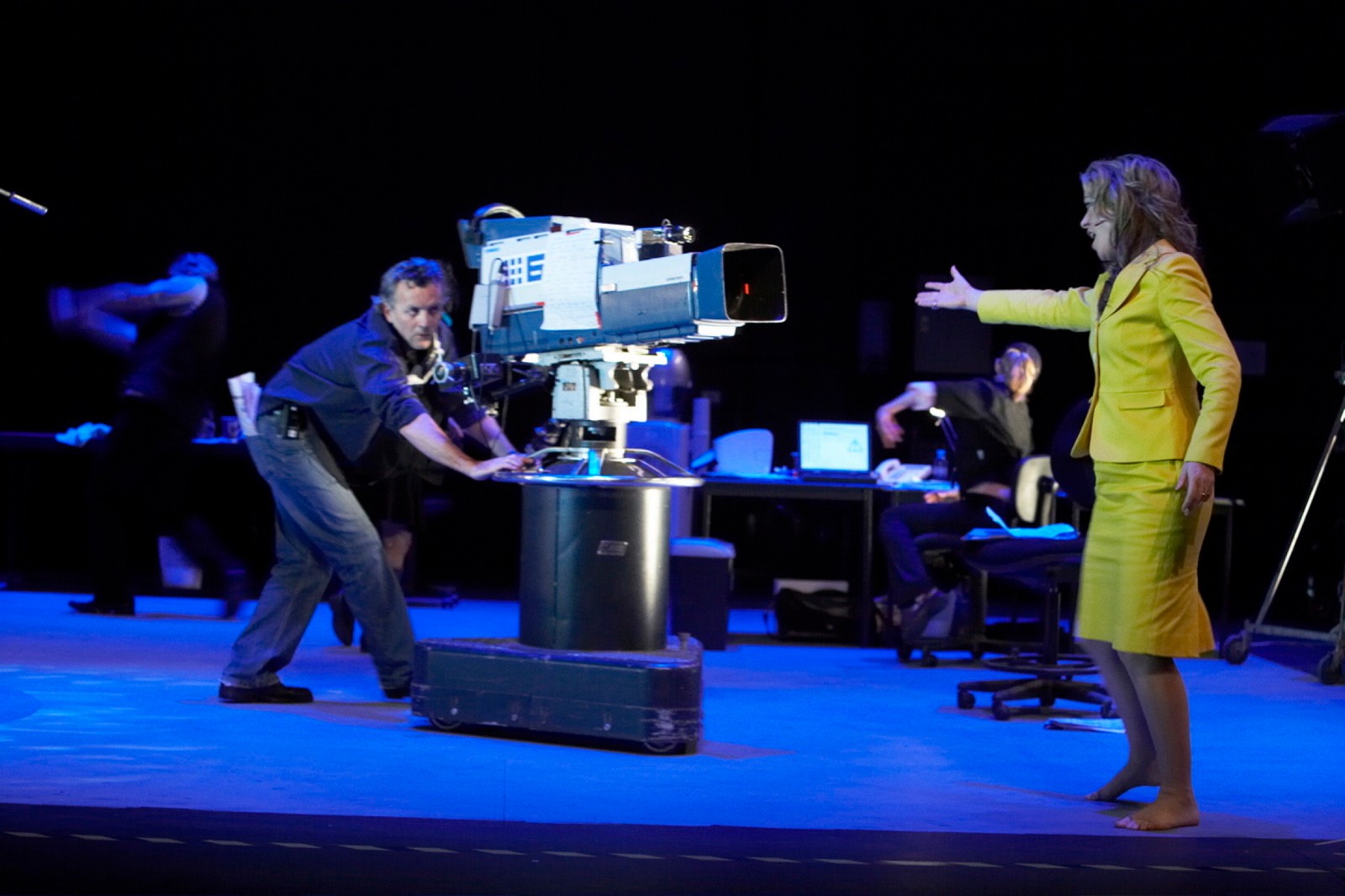 A man behind a TV camera approaching a woman singing with outstretched arm directed towards the camera