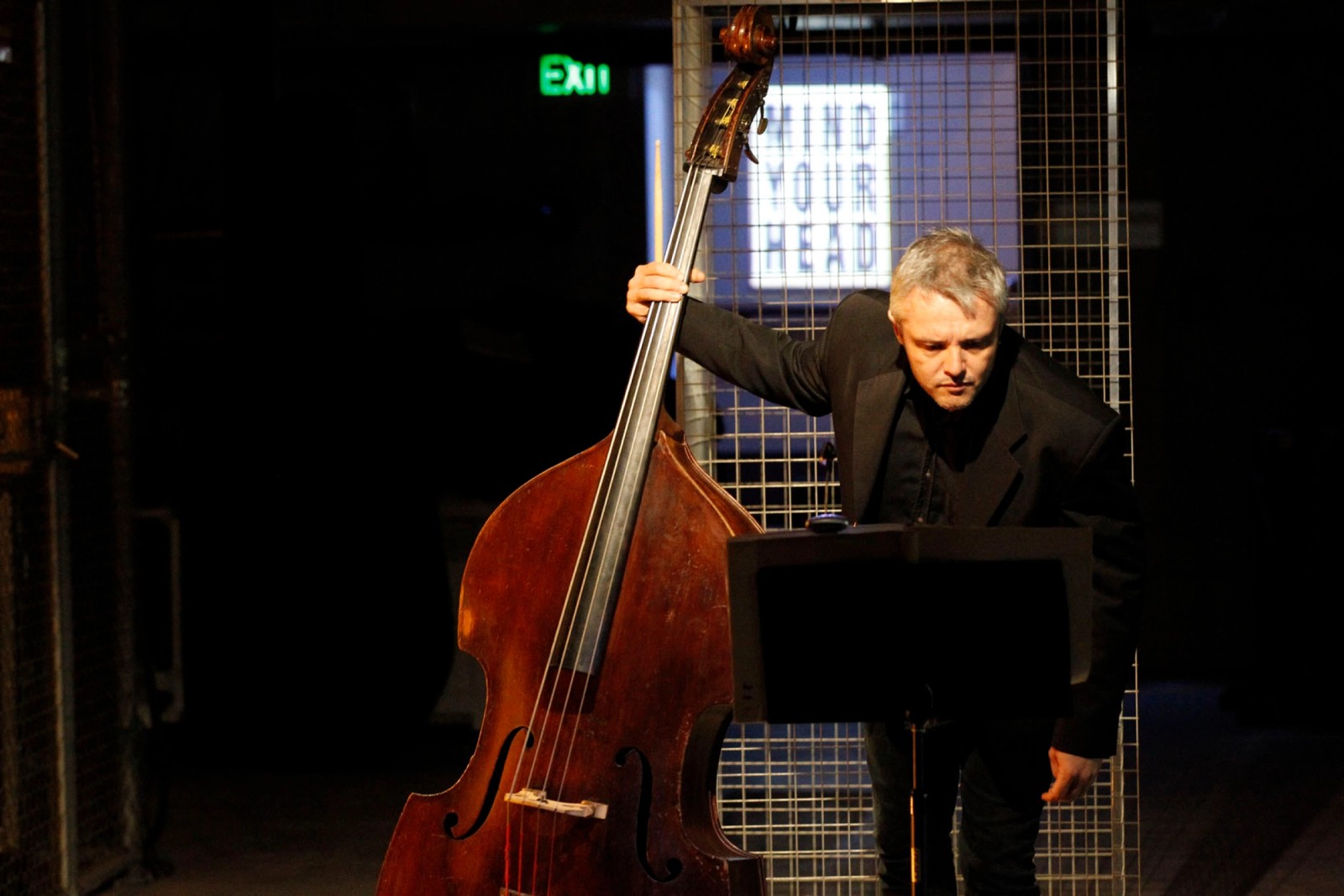 A man holding a double bass leans over a music stand as part of Captives of the City by Chamber Made