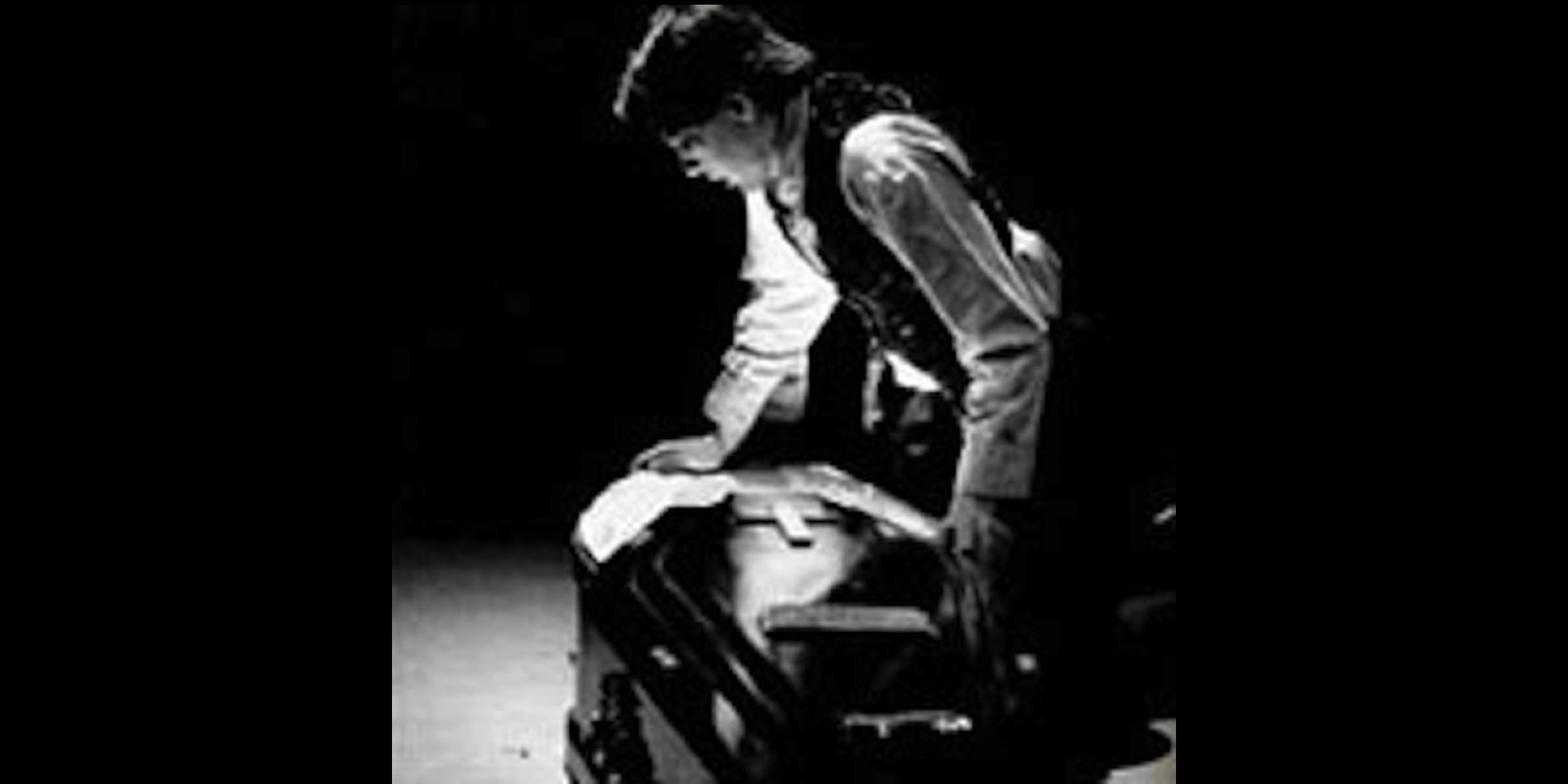 A man wearing shirt sleeves and a vest standing over a coffin