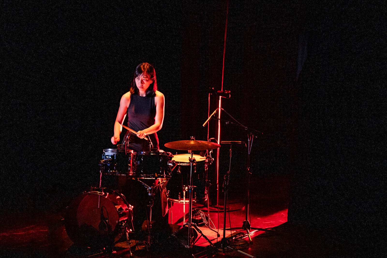 Woman in a dark space playing the drumkit as part of One Day We'll Understand.