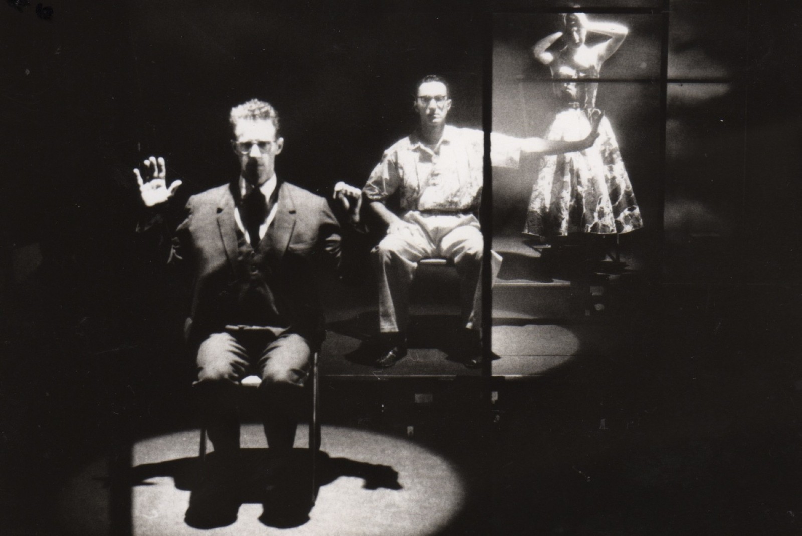 Three figures progressively further upstage: two seated men and a woman standing towards the back