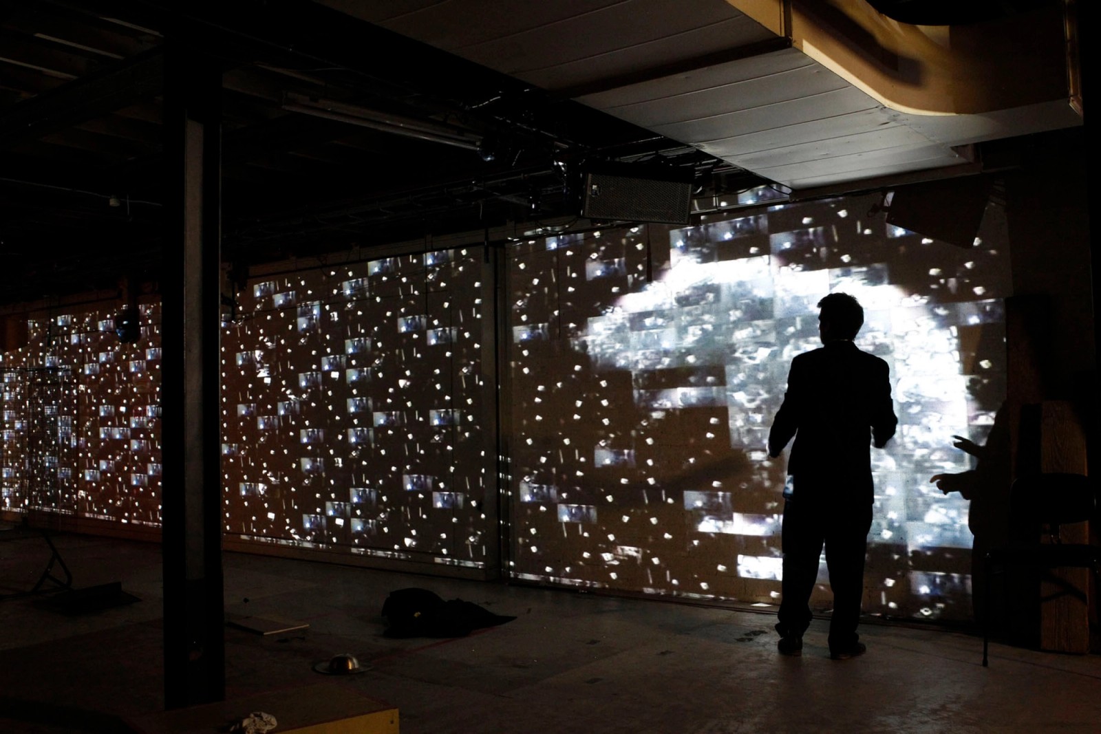 A man stands in front of a wall with a large projection of a rat and other lights as part of Captives of the City by Chamber Made