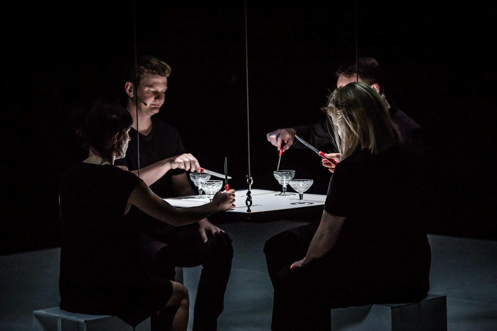 Four performers in low light sit around a square table as part of Permission to Speak by Chamber Made
