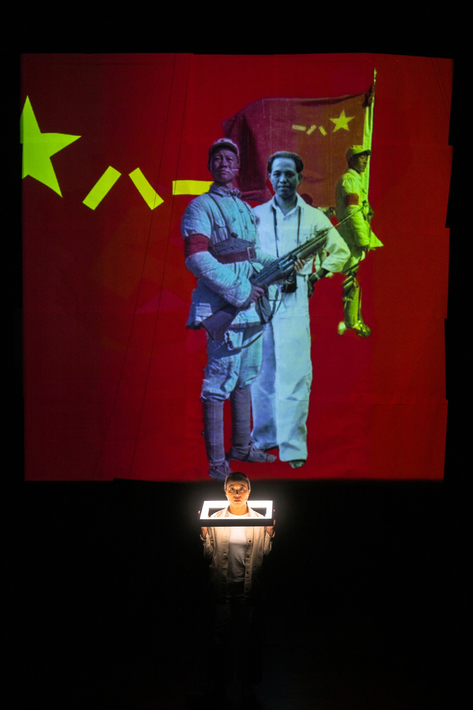 Woman standing on stage in front of large screen with projections of a Chinese Nationalist soldier as part of One Day We'll Understand.