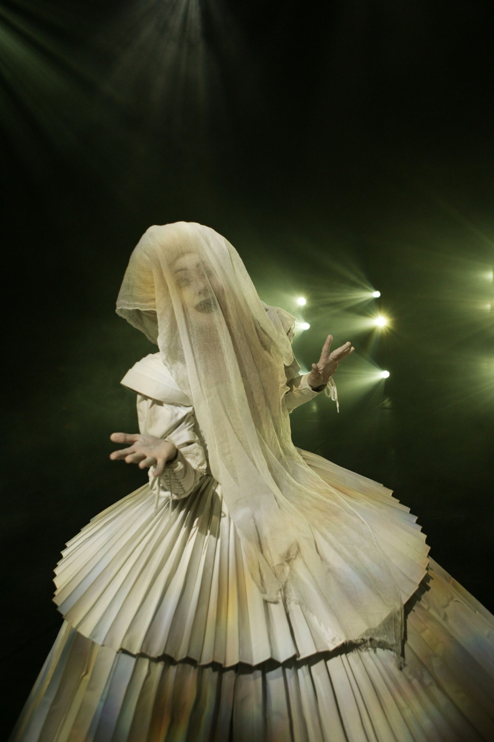 Woman in a white pleated gown with white baroque wig and sheer white shawl over her face