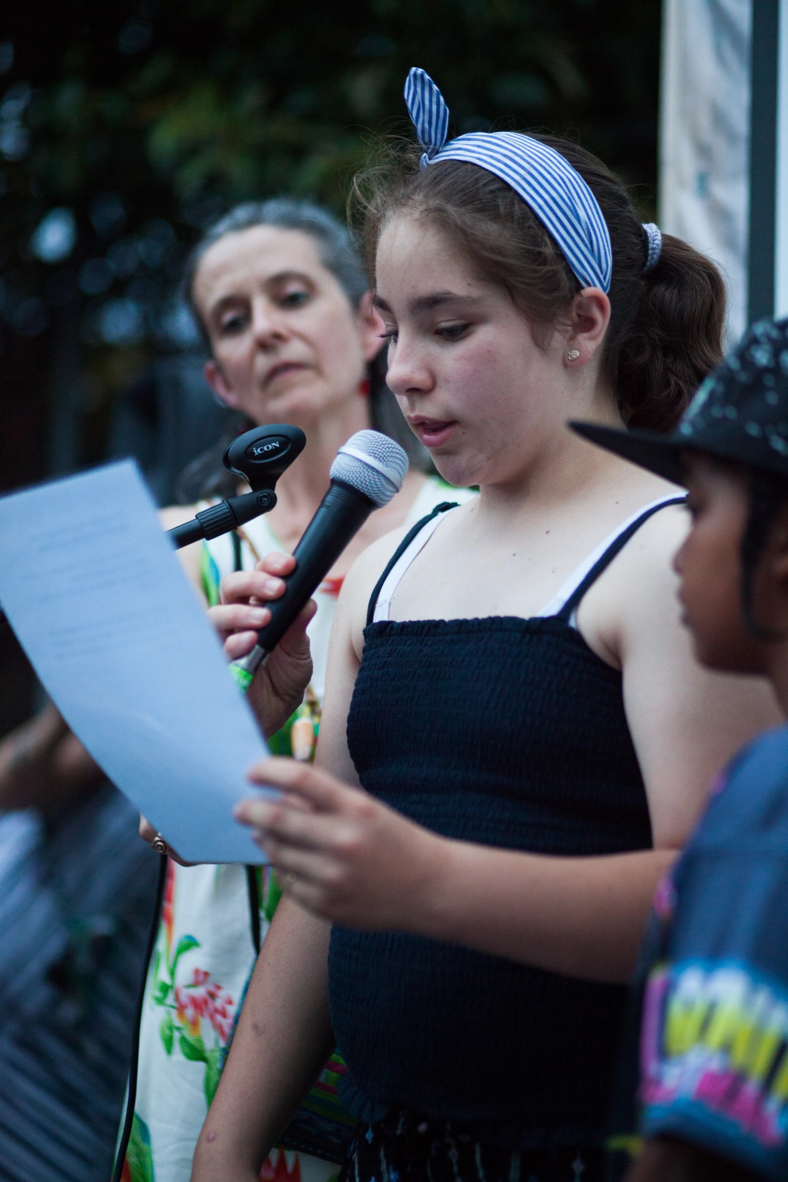 A girl performs with a microphone while a child and woman watch on as part of The Chamber Made Venny Celebration 2018