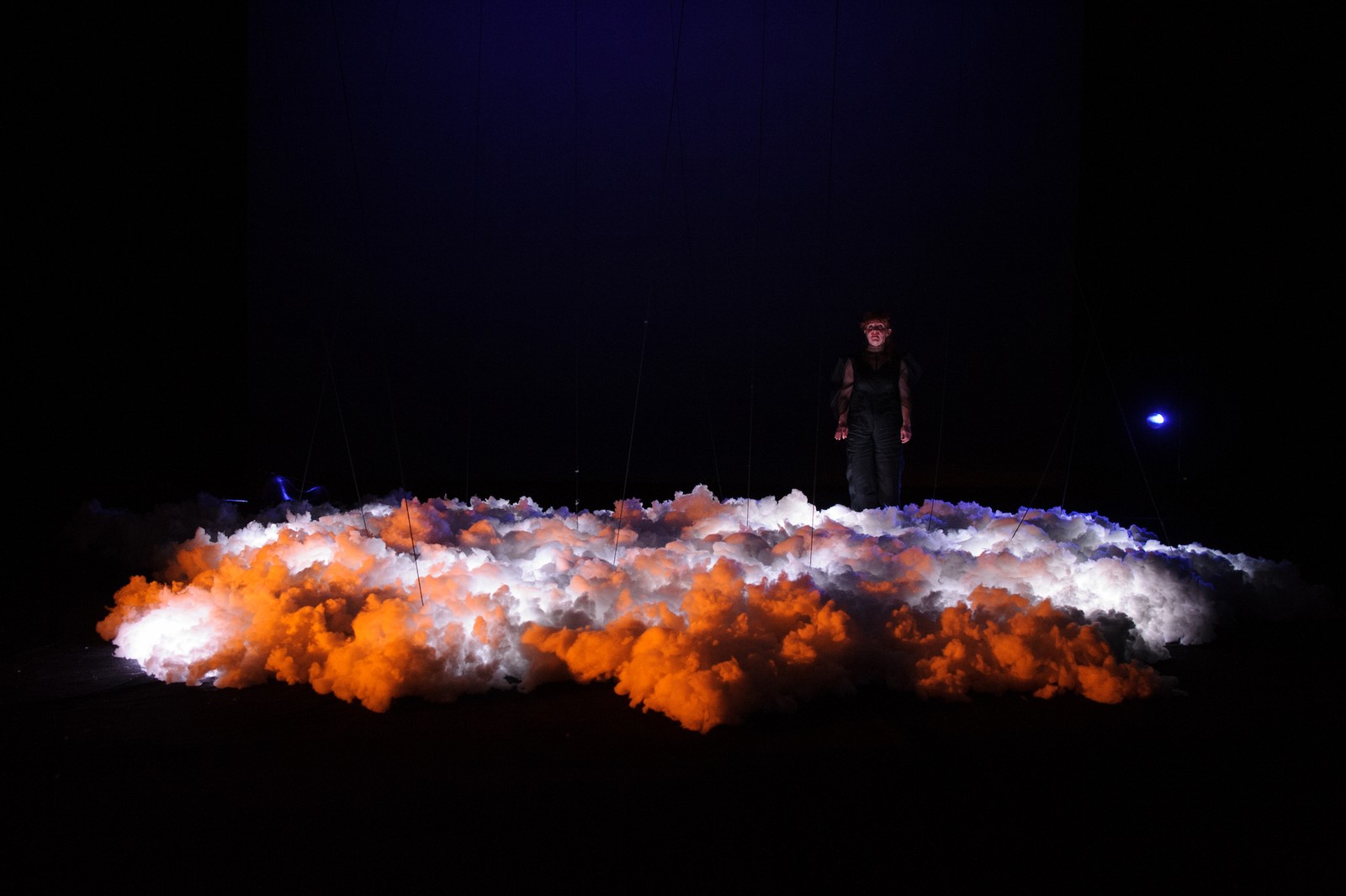 In a darkened space a woman stands above a mass of clouds as part of The Nervous Atmosphere by Zoe Barry and Chamber Made