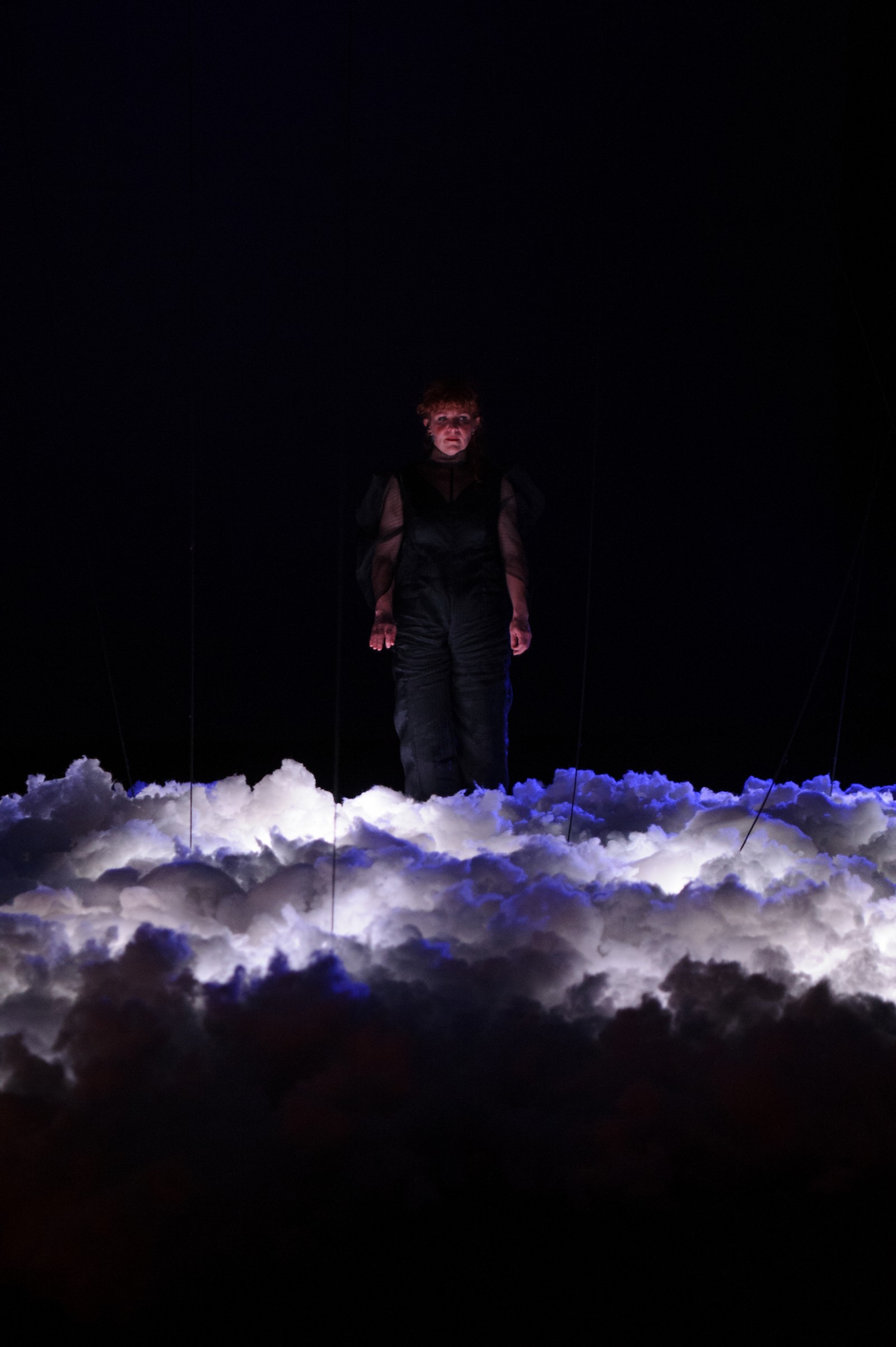 n a darkened space a woman stands above a mass of clouds as part of The Nervous Atmosphere by Zoe Barry and Chamber Made