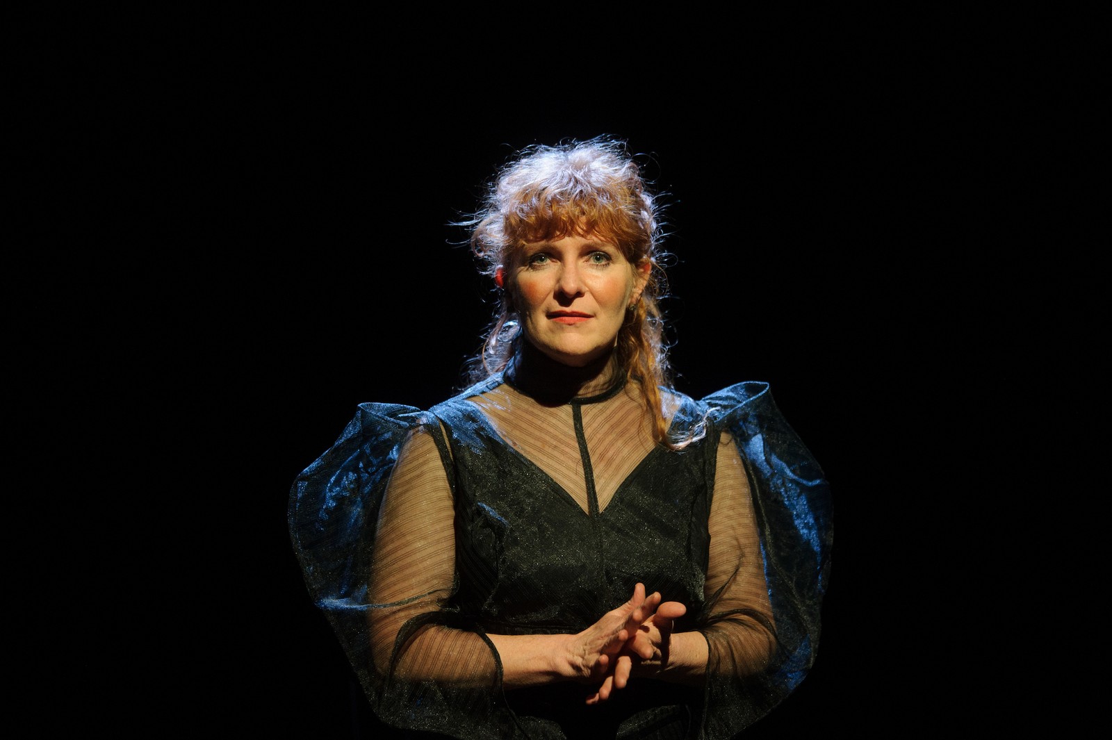In a darkened space a woman dressed in black looks to the audience as part of The Nervous Atmosphere by Zoe Barry and Chamber Made