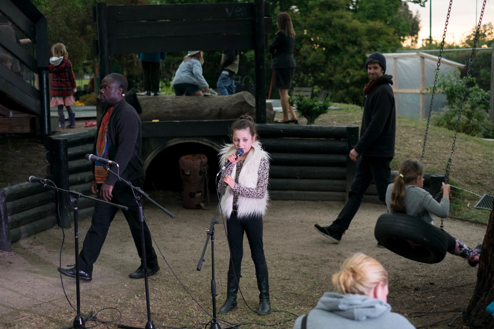 A girl performs at a microphone in a playground with others around as part of Chamber Made's The Venny Imagine a Place 2017