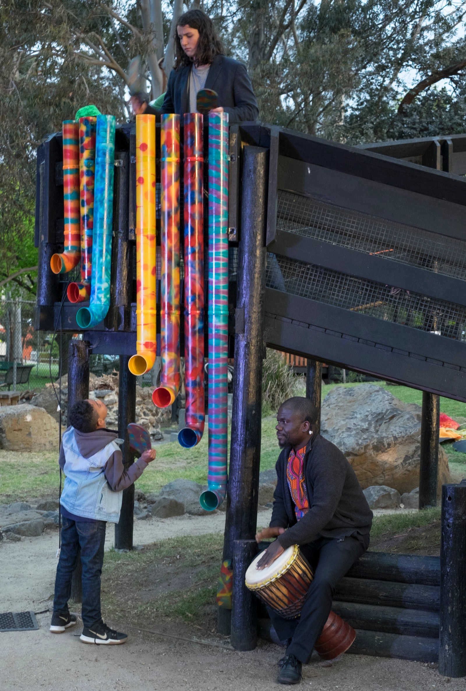 A bright tube structure with two young people and a man drumming as part of Chamber Made's The Venny Imagine a Place 2017