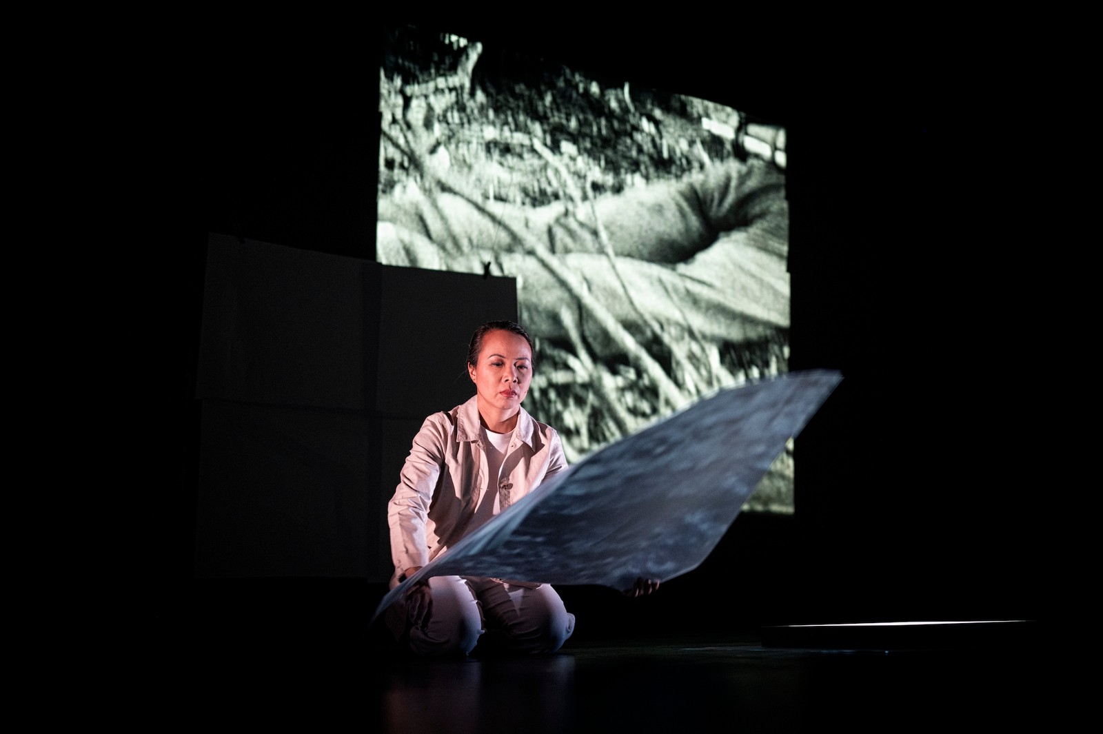 Image of a woman kneeling on stage with a projection on a large screen behind her as part of One Day We'll Understand.