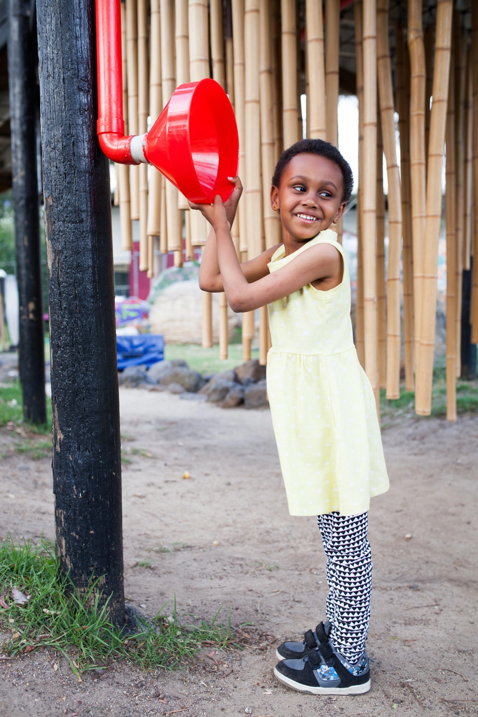 A girl playing with a red plastic sound tube installation as part of The Chamber Made Venny Celebration 2018