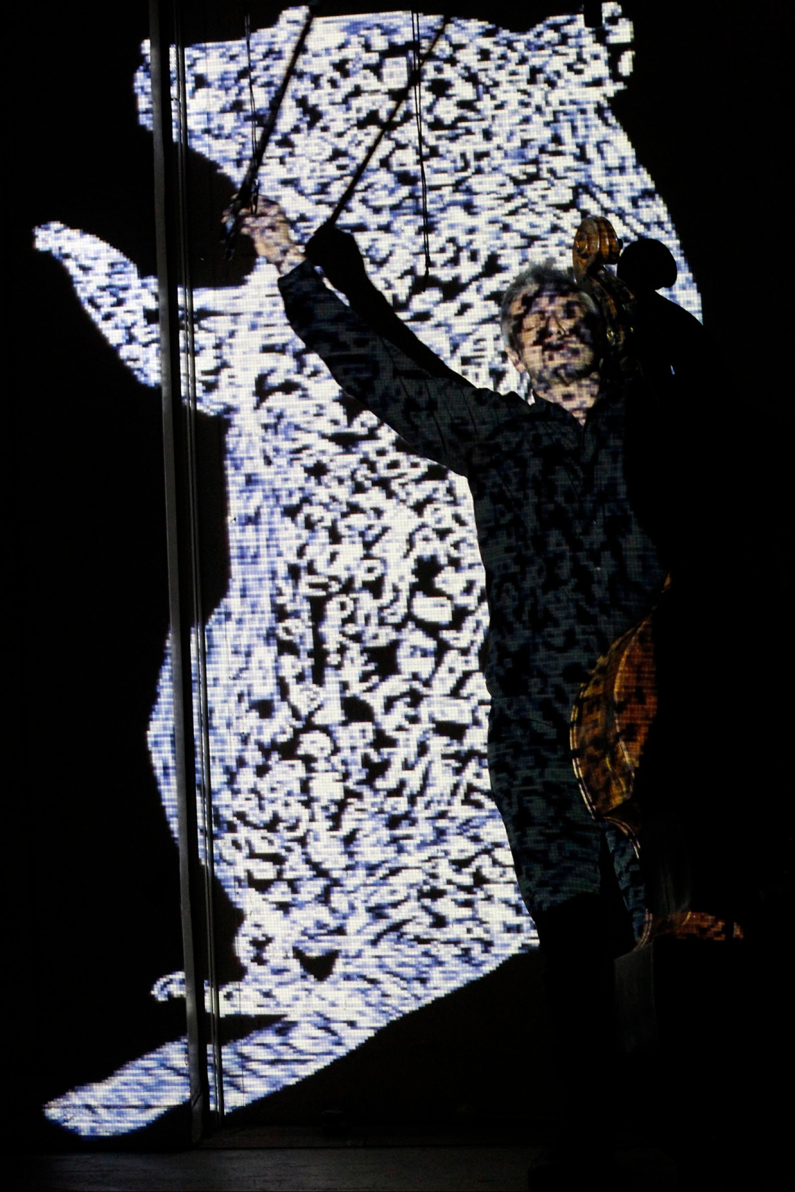A man with a double bass raises his arm in front of a projection of a giant rat as part of Captives of the City by Chamber Made