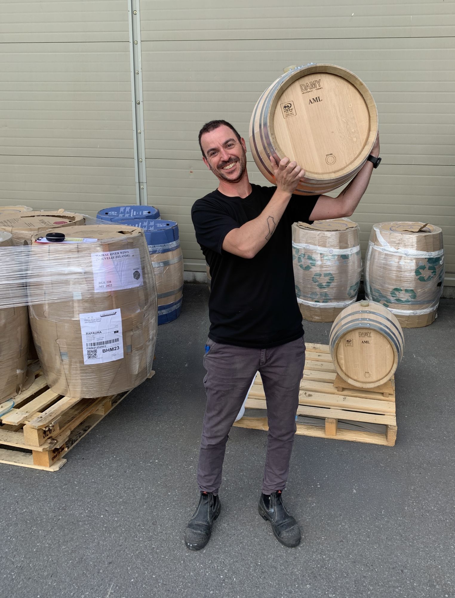 Tommaso Tadiello sorridente con una barrique sulla spalla, tra le botti appena consegnate in cantina