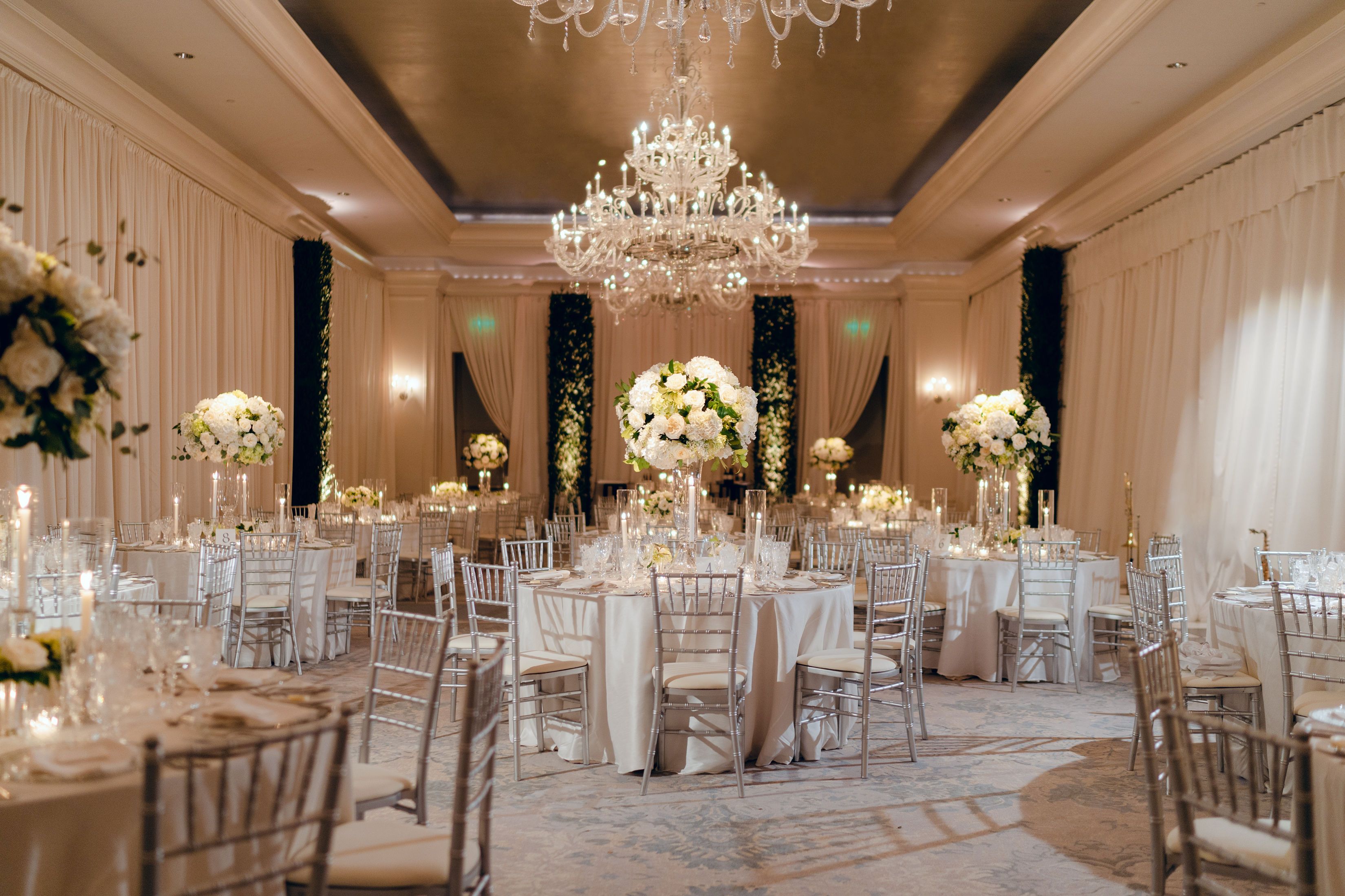 An elegant ballroom decorated for a wedding reception with Chiavari chairs. linens, and stunning white floral arrangements.