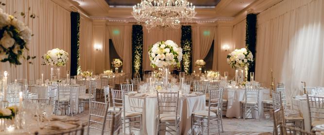 An elegant ballroom decorated for a wedding reception with Chiavari chairs. linens, and stunning white floral arrangements.