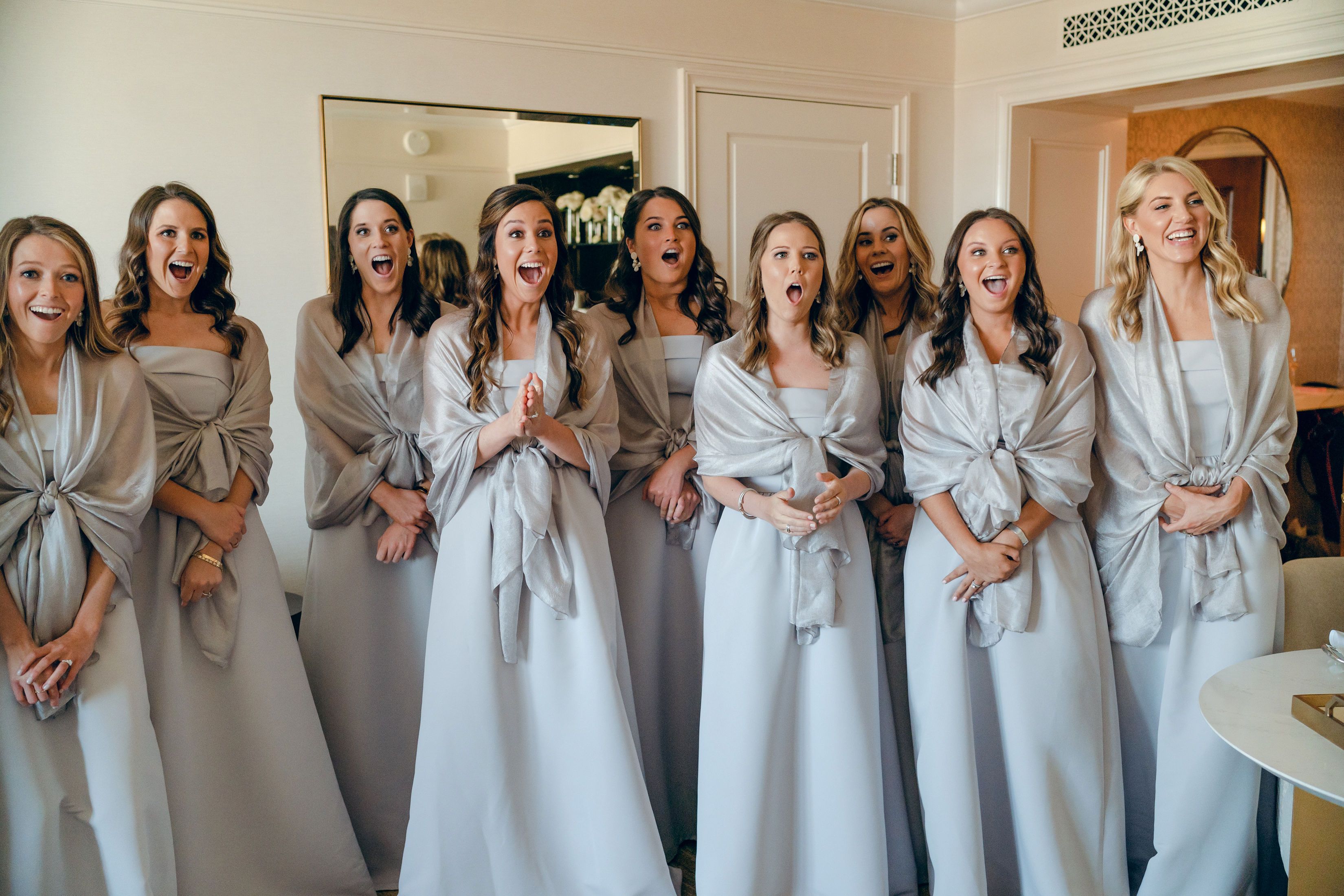 A group of bridesmaids react to their first look of a bride in her wedding dress.