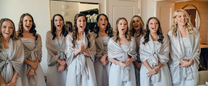 A group of bridesmaids react to their first look of a bride in her wedding dress.