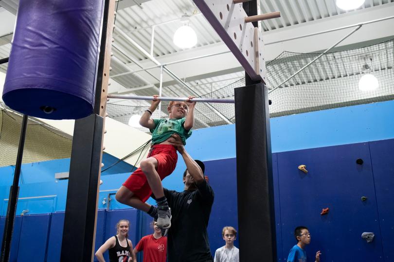 Coach helping a child hanging from a monkey bar