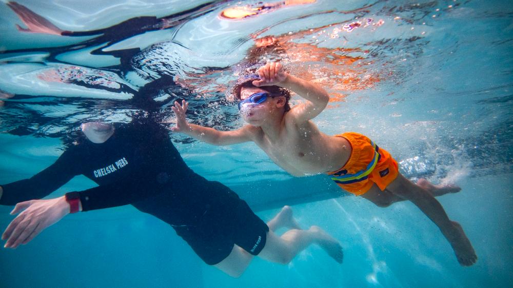 Child swimming towards pool wall with swim instructor in pool
