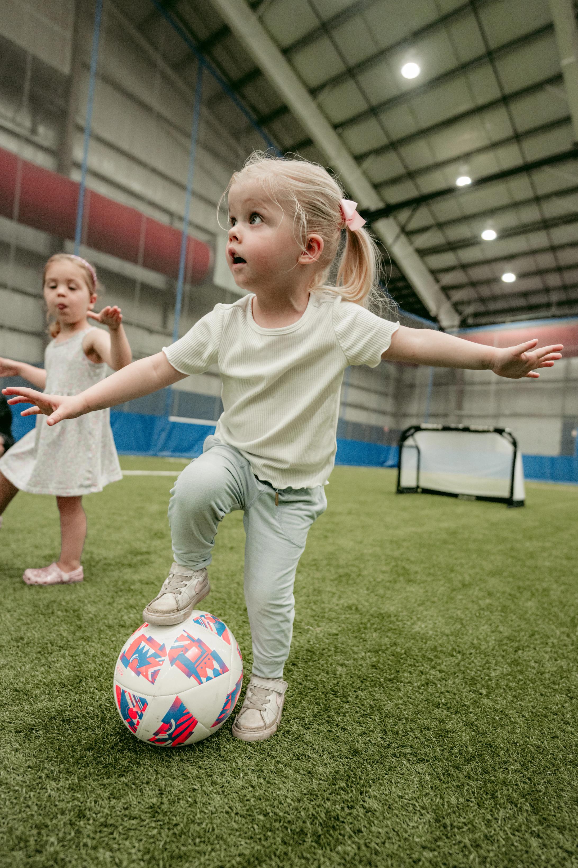 preschool girl standing on soccer ball