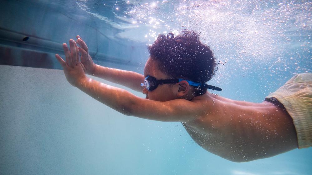 Child swimming towards pool wall with swim instructor in pool