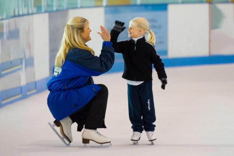 Young skater high fiving coach on ice
