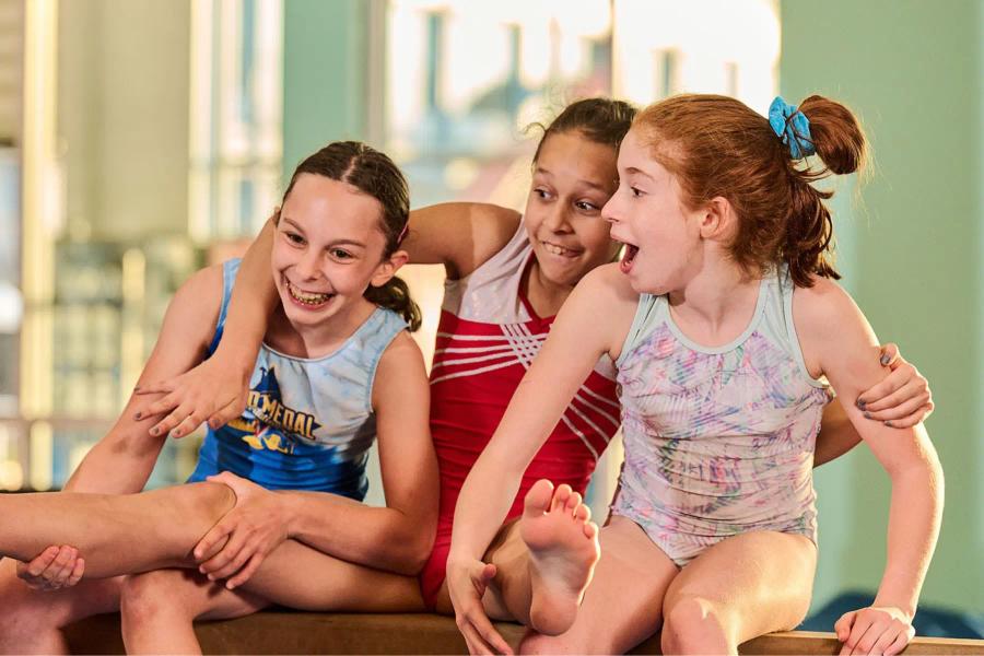 3 girls smiling on the gymnastics beam
