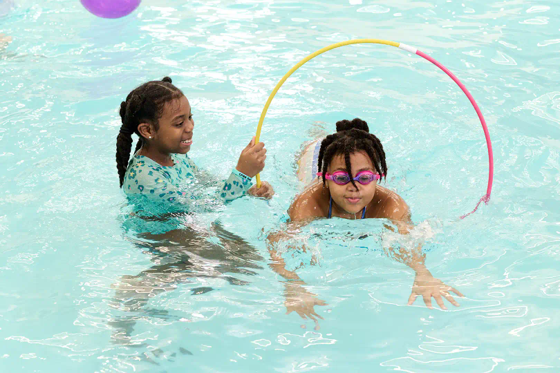 Two girls swimming in pool, playing games. 