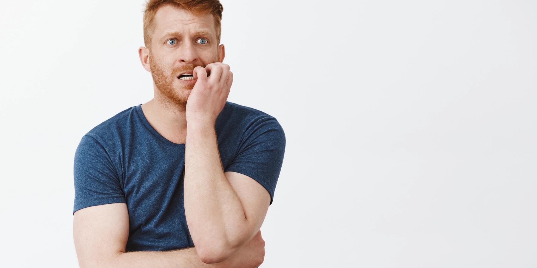 Töprengő fiatal férfi kék pólóban a körmét rágja