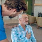 Sötét hajú orvos hajol egy idősödő, kaukázusi férfi felé, aki mellkasi fájdalmat érez.