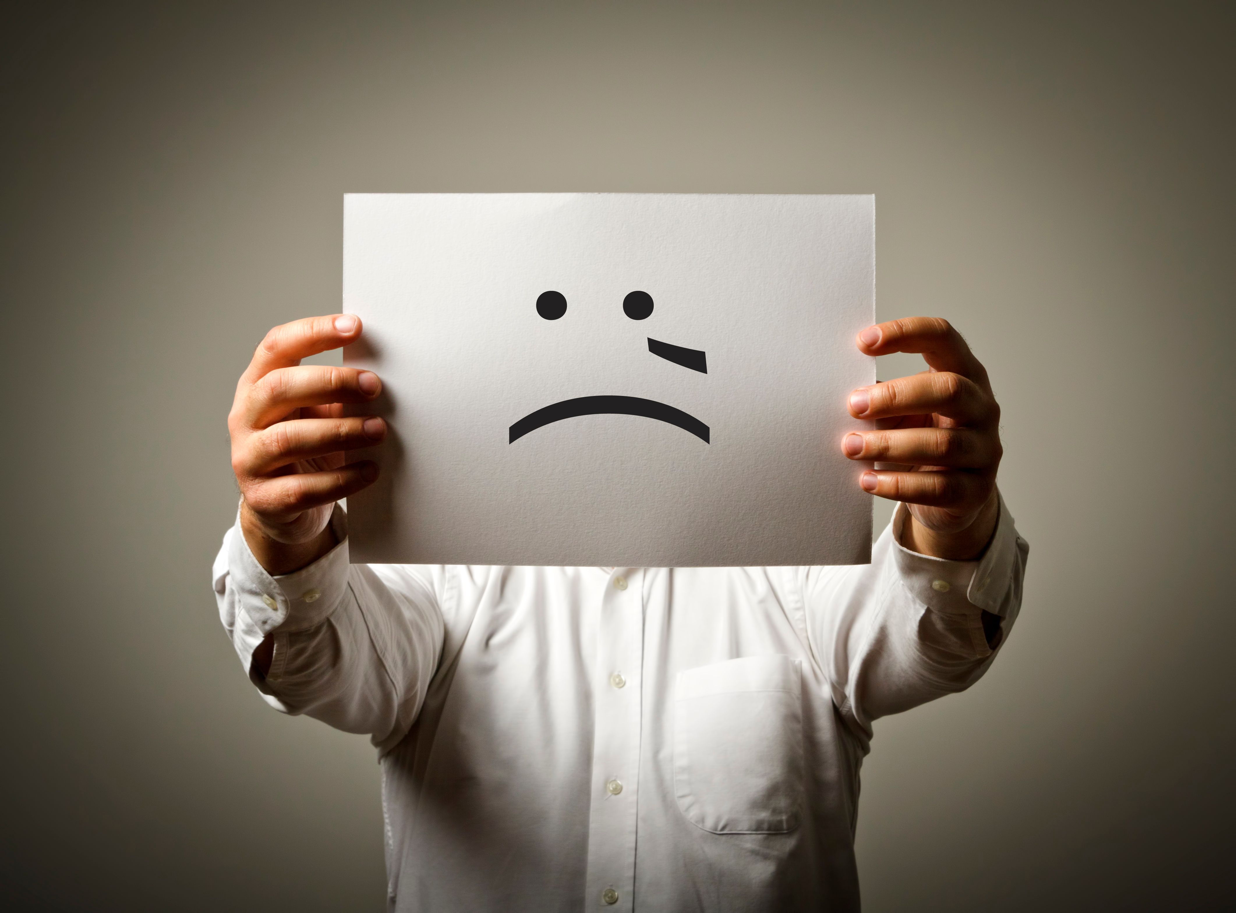 Férfi kezében papírral arcát takarja, miközben áll a bézs háttér előtt