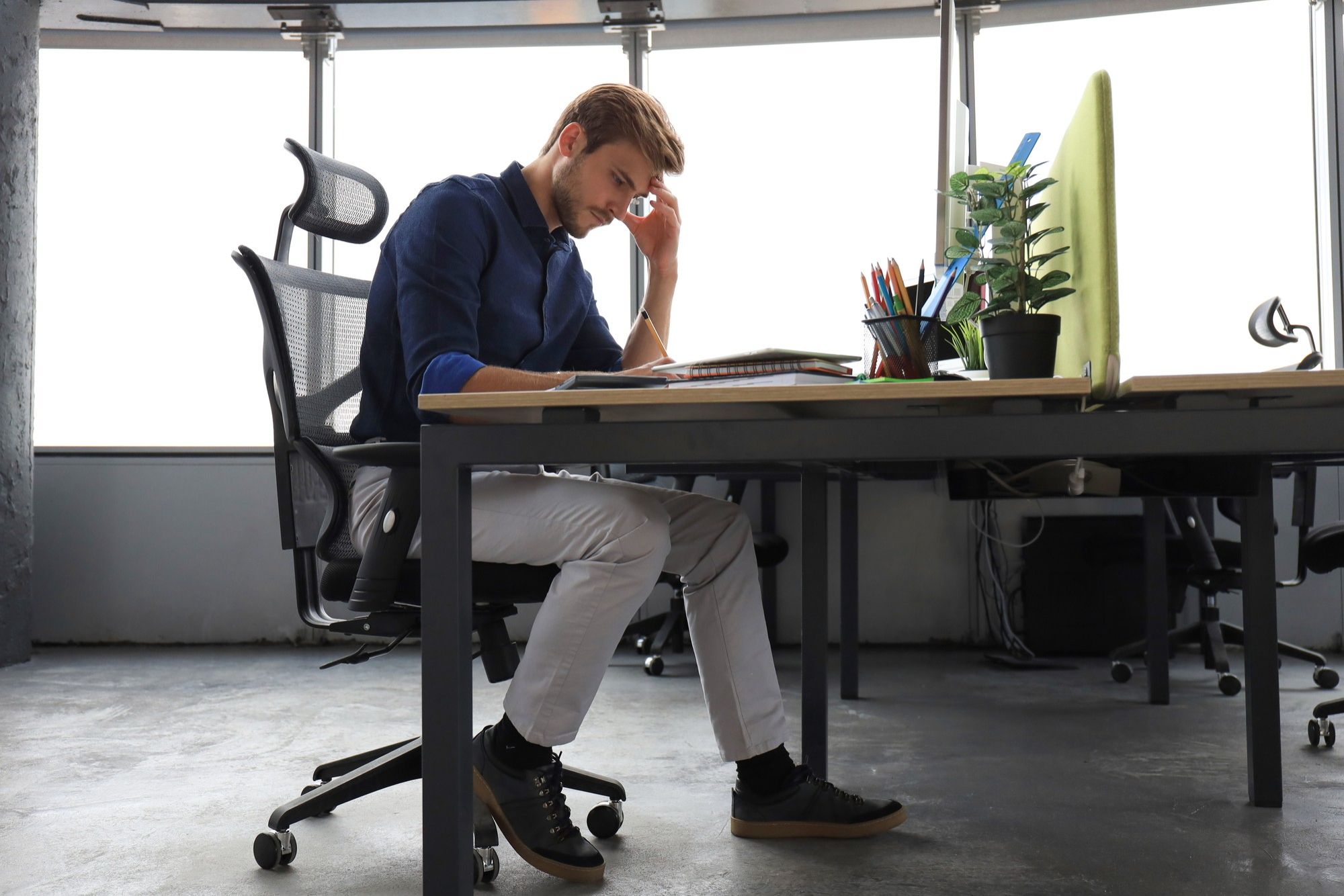 Helytelenül ülő férfi, az asztalra dőlve, miközben füzetét nézi