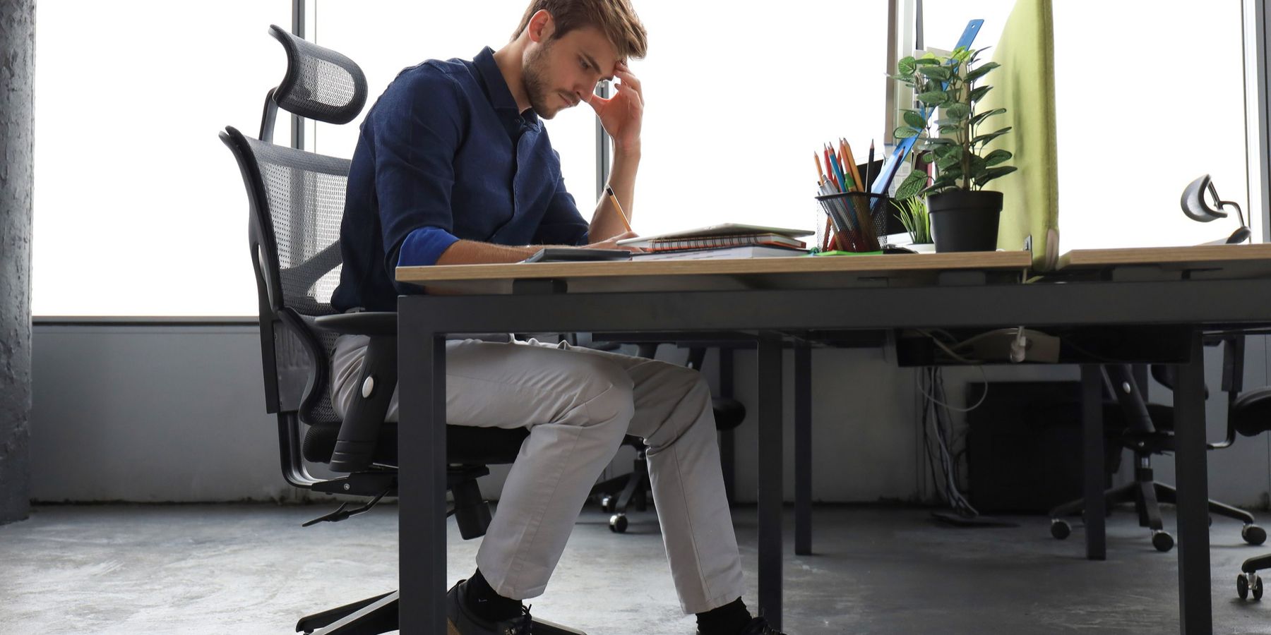 Helytelenül ülő férfi, az asztalra dőlve, miközben füzetét nézi