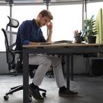 Helytelenül ülő férfi, az asztalra dőlve, miközben füzetét nézi